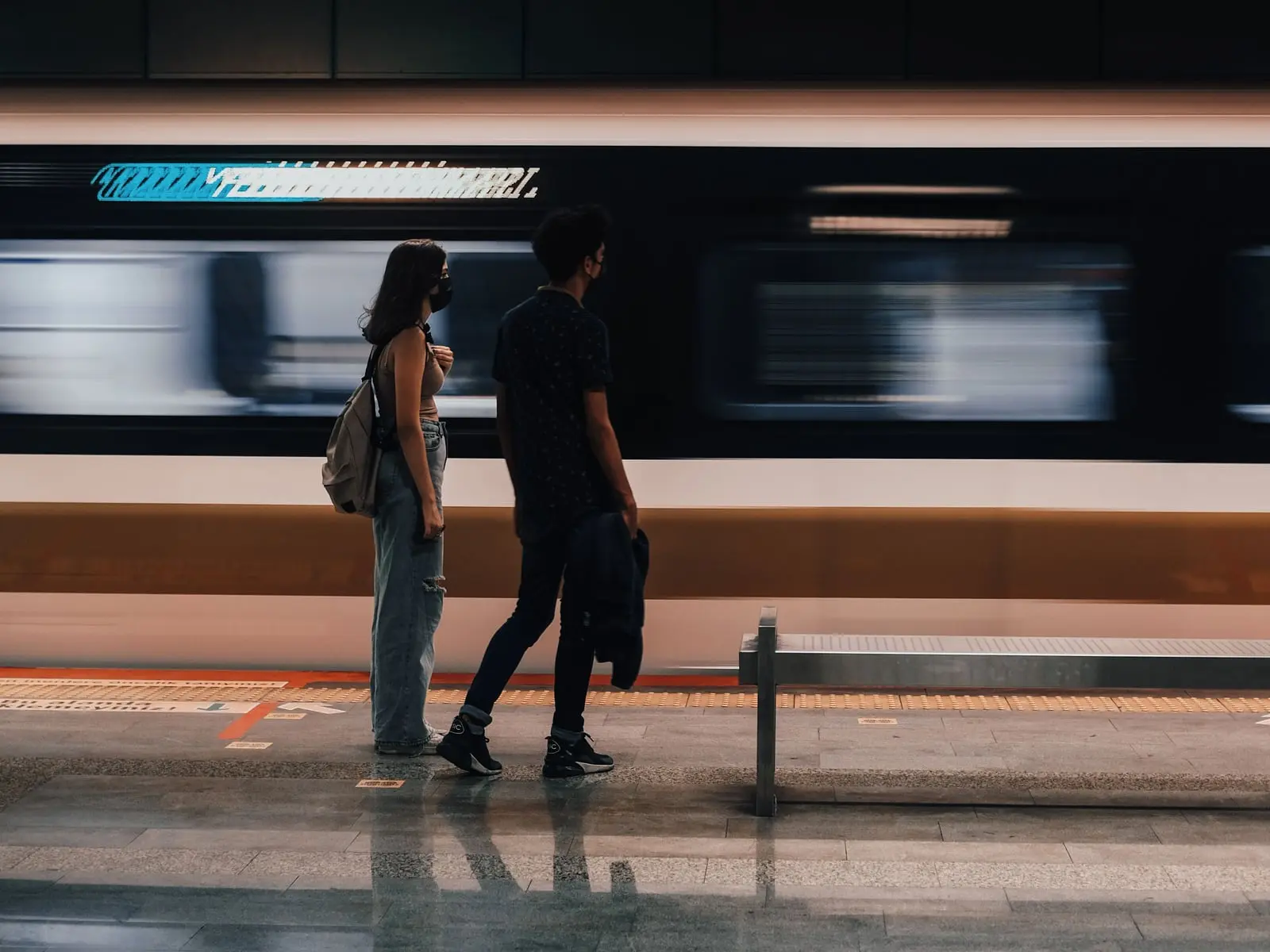 A couple standing on a train platform as a train rushes past